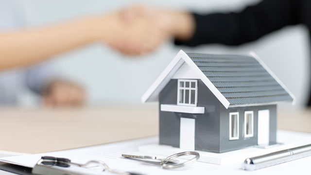 Photo of house with realtor keys  and two people shaking hands